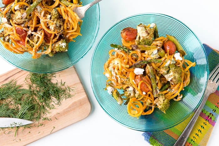 2 blue plates with Balsamic Roasted Spring Vegetables with Butternut Squash Noodles next to a wooden cutting board with freshly chopped dill