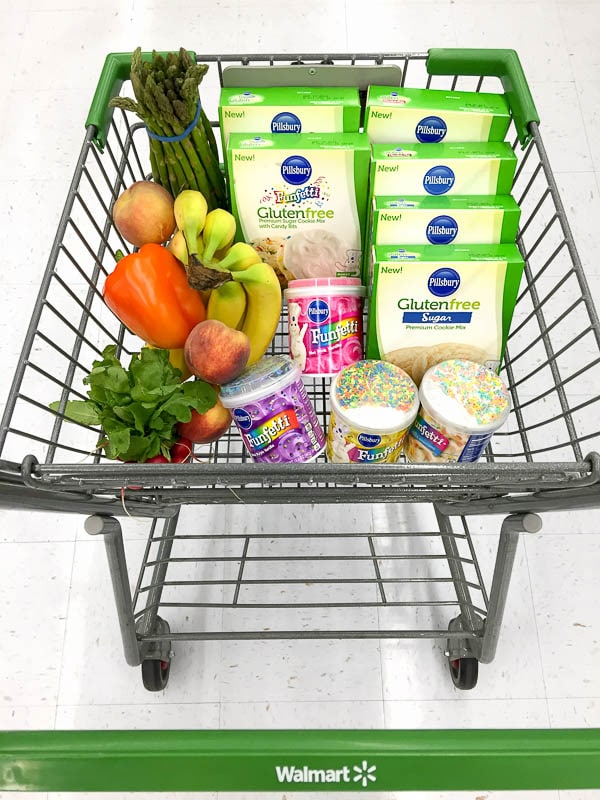 Walmart shopping cart full of Pillsbury gluten-free cake mixes, frostings, and fresh produce