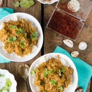 2 white plates of Seychelles-style Coconut Chicken Curry surrounded by some of the ingredients used to make it