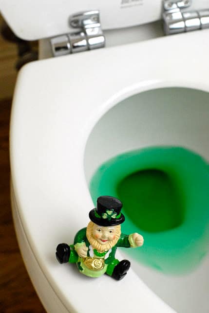 St. Patrick\'s Day antics - leprechaun sitting on the edge of a toilet with green water