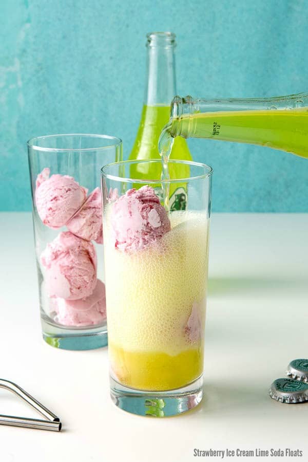 pouring lime soda into a fountain glass filled with strawberry ice cream to make strawberry lime ice cream floats