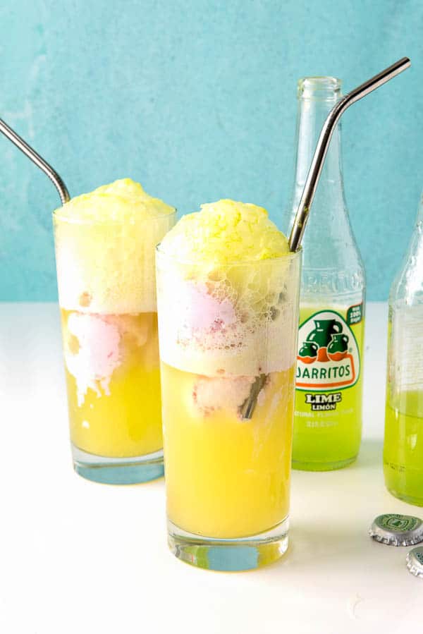 2 tall soda fountain glasses of Strawberry Ice Cream Lime Soda Floats with silver straws and bottles of lime soda next to the glasses