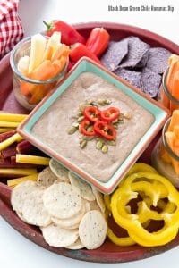 platter holding fresh vegetables and chips for dipping and a bowl of gluten free black bean green chile hummus dip