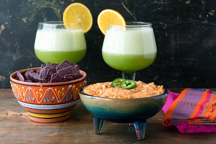 bowl of Chorizo con Queso Dip next to a bowl of Blue Corn Chips, with 2 Honeydew Margaritas behind the bowls