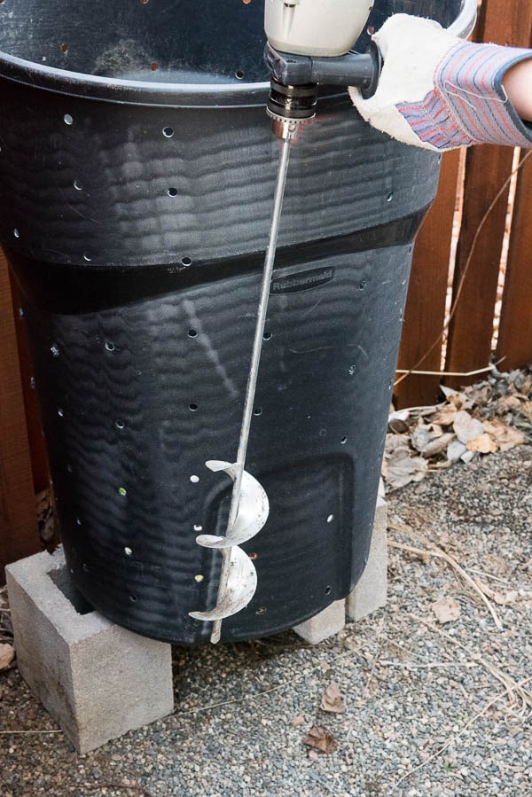 power drill with an auger bit attached to it and a home composting can behind it