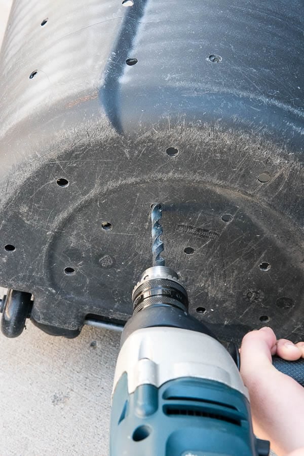 person holding a drill that\'s making holes into the bottom of a homemade composting can