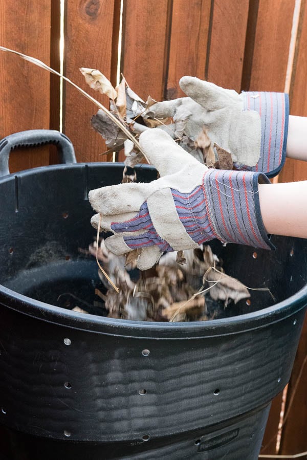gloved hands adding leaves to a homemade compost can