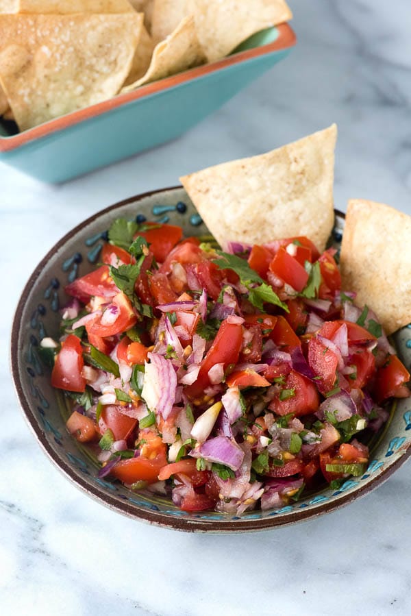 bowl of homemade tortilla chips and bowl of pico de gallo salsa with a couple of chips in it.