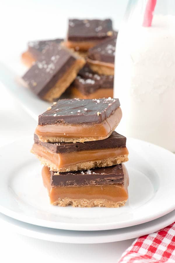 a stack of white dessert plates holding no bake chocolate millionaire shortbread bars