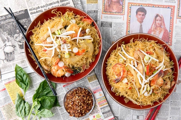 2 bowls of Singapore Street Noodles on top of a Singapore newspaper. Chopsticks sit on the side of one bowl.