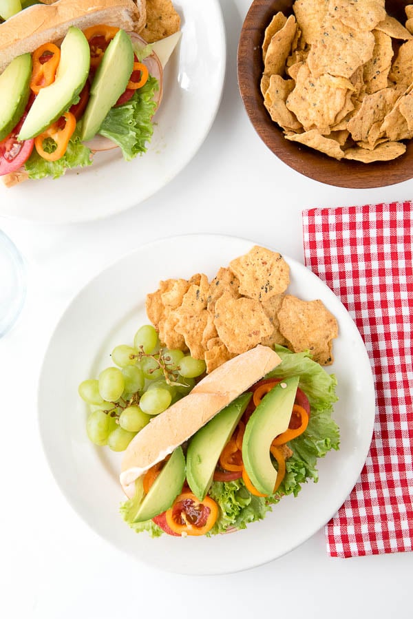 2 white plates with Southwestern Sub Sandwiches with chipotle mayo. Also on the plates: fresh grapes and gluten free chips