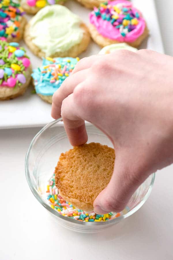 dipping a frosted cookie in sprinkles