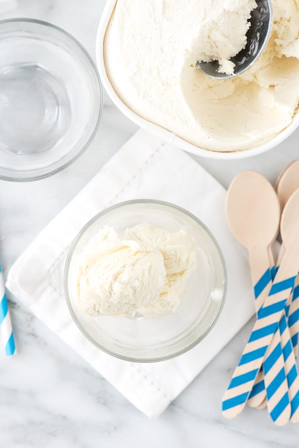 vanilla ice cream in an ice cream float glass next a container of the ice cream and blue striped spoons for serving