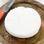 titled photo: Homemade Paneer - overhead image showing a wheel of Indian paneer cheese on a cutting board