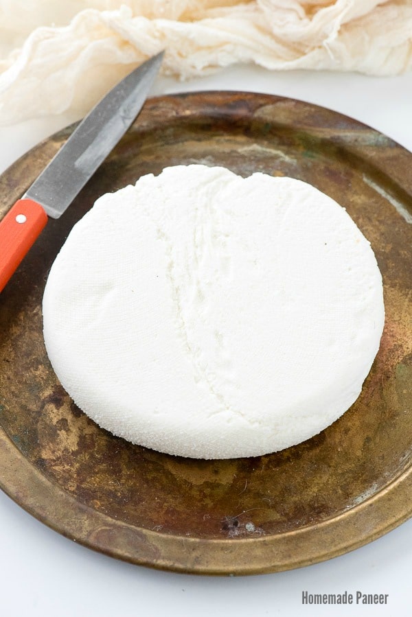 titled photo: Homemade Paneer - overhead image showing a wheel of Indian paneer cheese on a cutting board