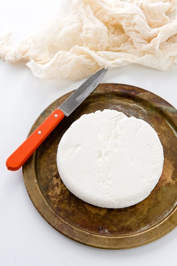 overhead image of a wheel of homemade paneer cheese sitting on a round platter with a knife