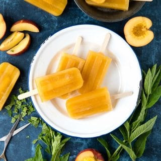Peach Ginger Mint Paletas {popsicles} on a white plate, surrounded by fresh peaches and more popsicles