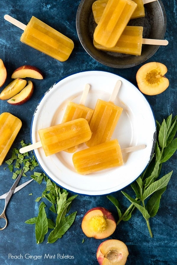 Peach Ginger Mint Paletas {popsicles} on a white plate, surrounded by fresh peaches and more popsicles