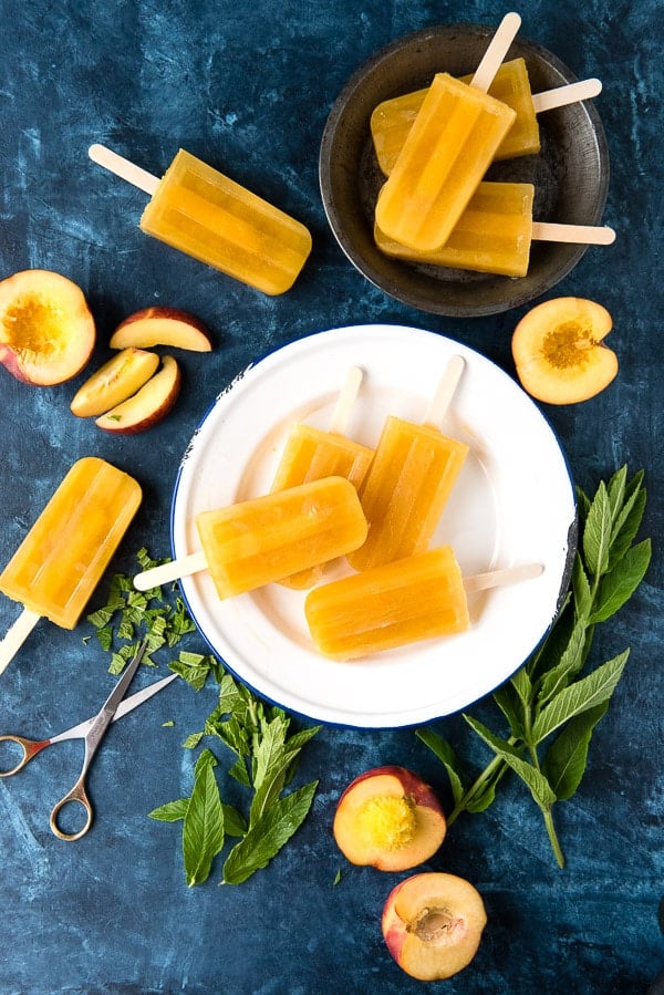Peach Ginger Mint Paletas {popsicles} on a white plate, surrounded by fresh peaches and more popsicles