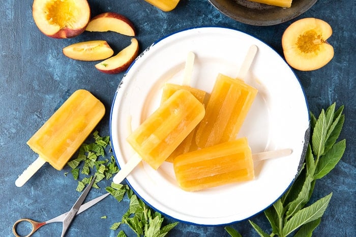 golden colored peach ginger mint popsicles on a white plate