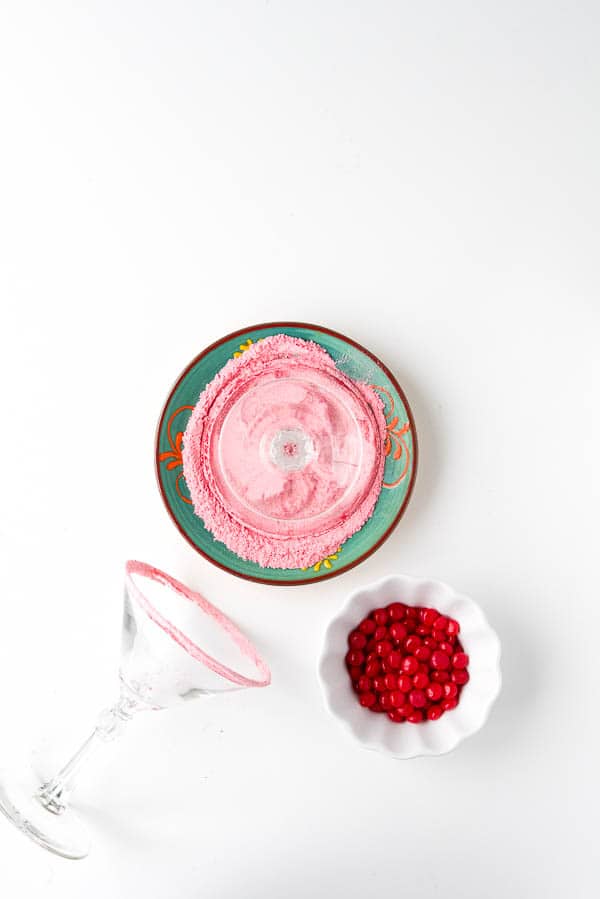 cocktail glass rimmed with crushed Red Hots candies. A bowl of the candies sits nearby