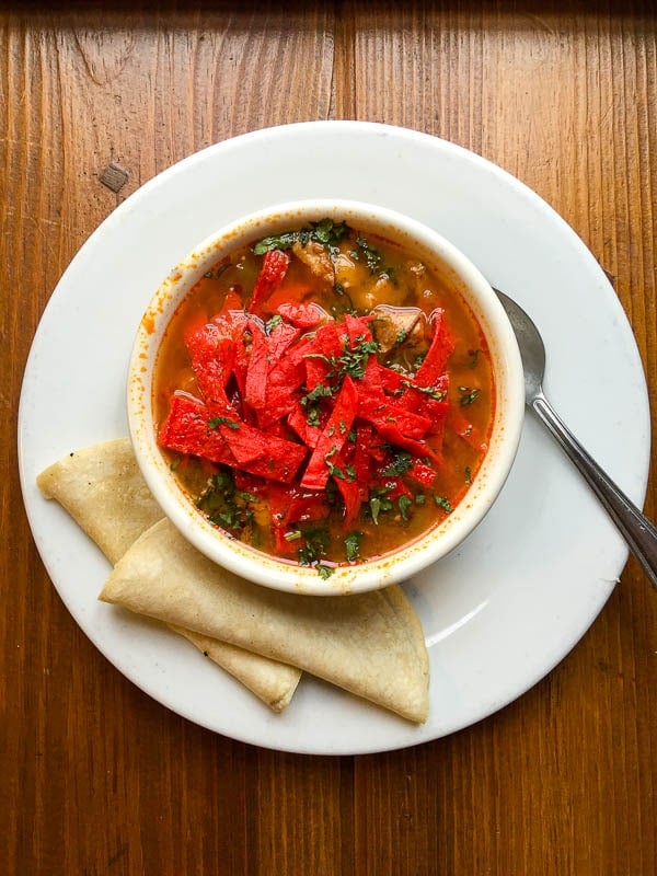 a white bowl of spicy Posole topped with red corn tortilla chips