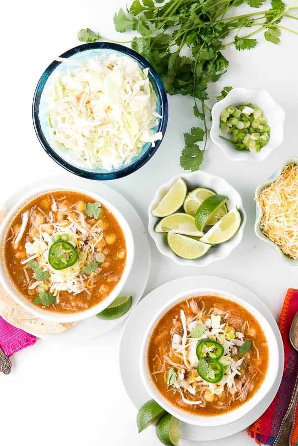 2 bowls of Posole Soup made in a slow cooker, surrounded by an assortment of garnishes for the hominy soup