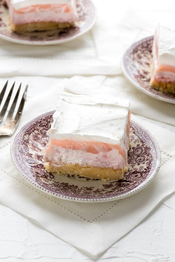 3 dessert plates with servings of layered strawberry cheesecake dessert on them.