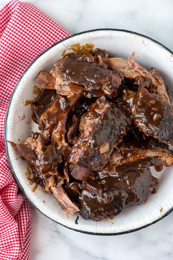 white bowl filled with saucy baby back ribs falling off of the bones