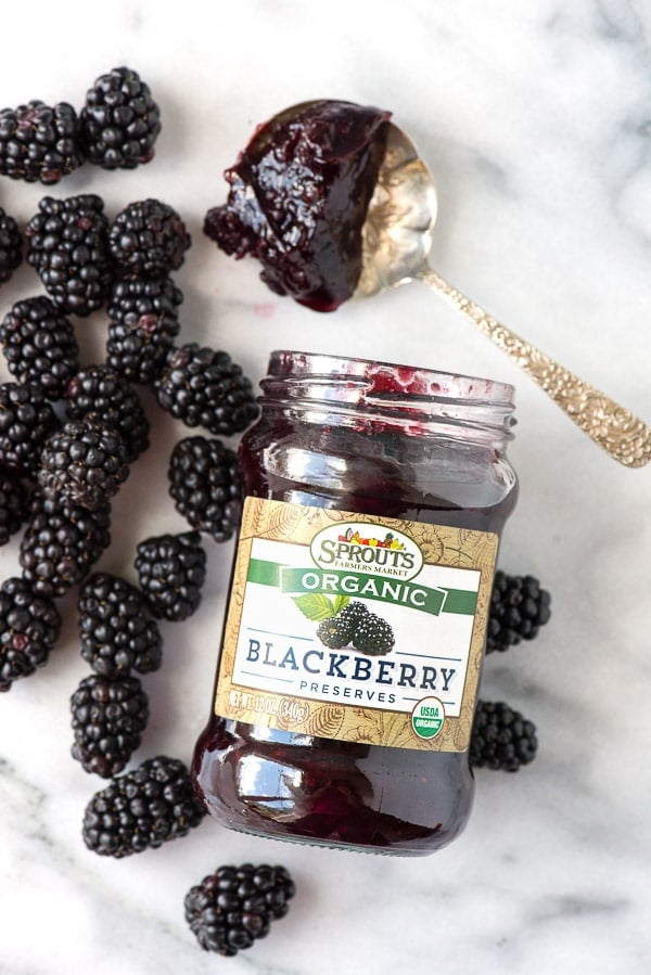 a jar of organic blackberry preserves surrounded by fresh blackberries. A spoonful of preserves sits nearby