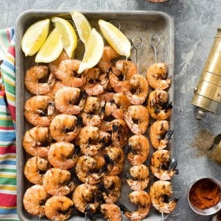 Grilled Spicy Salt and Pepper Shrimp Skewers on a baking sheet with lemon wedges