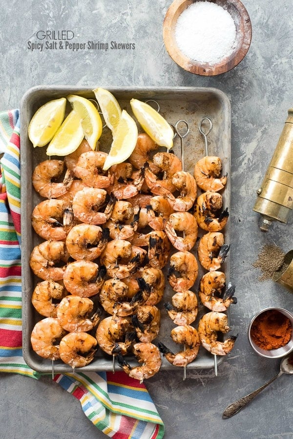 Grilled Spicy Salt and Pepper Shrimp Skewers on a baking sheet with lemon wedges