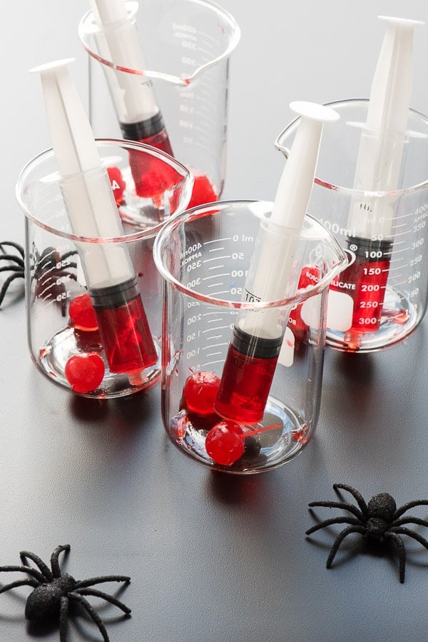 Beakers with large syringes of grenadine and maraschino cherries