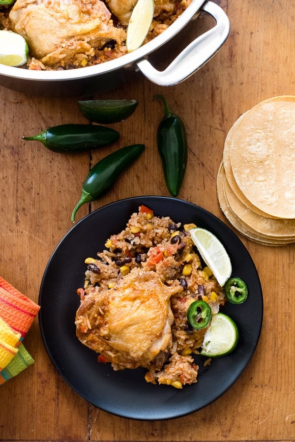 single serving of gluten-free Mexican Chicken and Rice Skillet on a black plate with fresh whole jalapeno peppers and part of the skillet