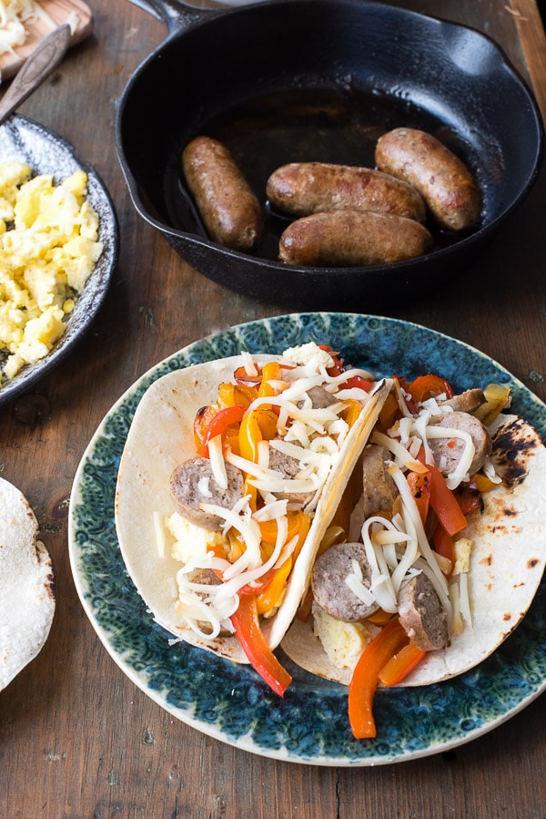 breakfast tacos with eggs and sausages in background