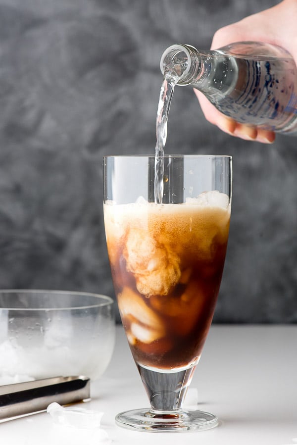 Pouring carbonated water into a glass of ice and coffee