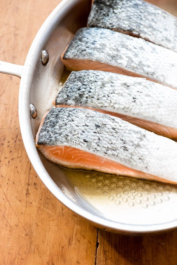 salmon filets cooking in a silver skillet