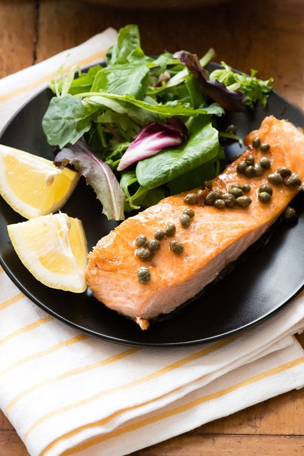 Pan Seared Salmon with Lemon and Capers on black plate with salad