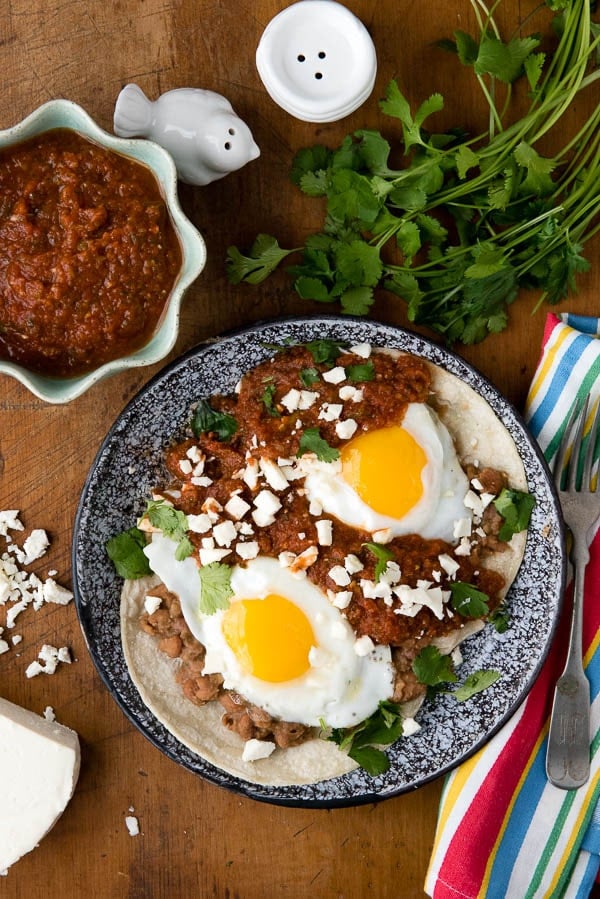 overhead image of a plate of Huevos Rancheros topped with fried eggs and a side of Rancheros sauce.