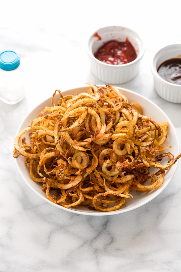 white bowl of spiralizer spicy baked curly fries with ketchup in ramekin