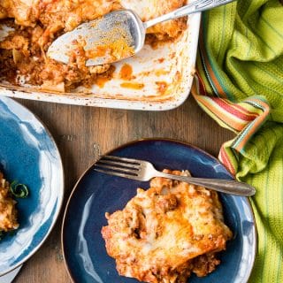 serving of meat lasagna on blue plate with part of white lasagna dish showing with serving scooped out