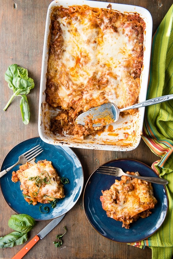 white baking dish of meat and cheese lasagna from overhead with servings on plates nearby