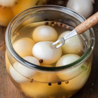 close up view of pickled pub onions in brine with an appetizer fork