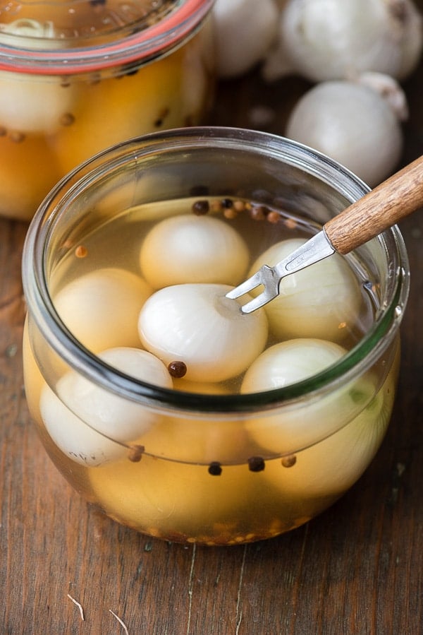 close up view of pickled pub onions in brine with an appetizer fork