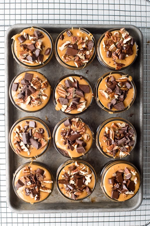 Overhead view of Jelly Jar Chocolate Turtle Brownies. Luscious individual brownies baked in jelly jars, topped with gooey caramel, pecans and chocolate chunks.