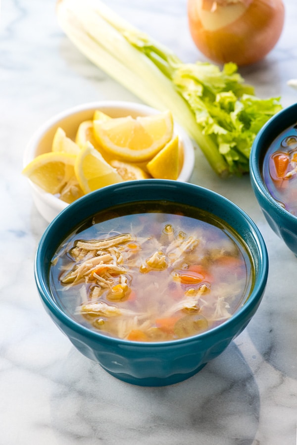 Blue bowl of hearty chicken soup with lemon wedges and celery in the background