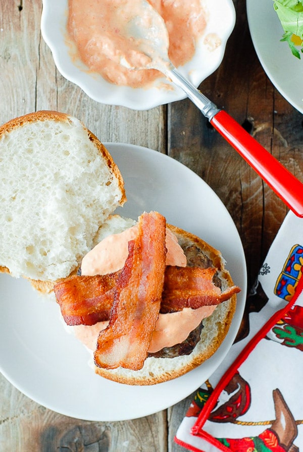 Crispy, fried bacon on top of a grilled hamburger with sriracha sour cream on a gluten-free bun 