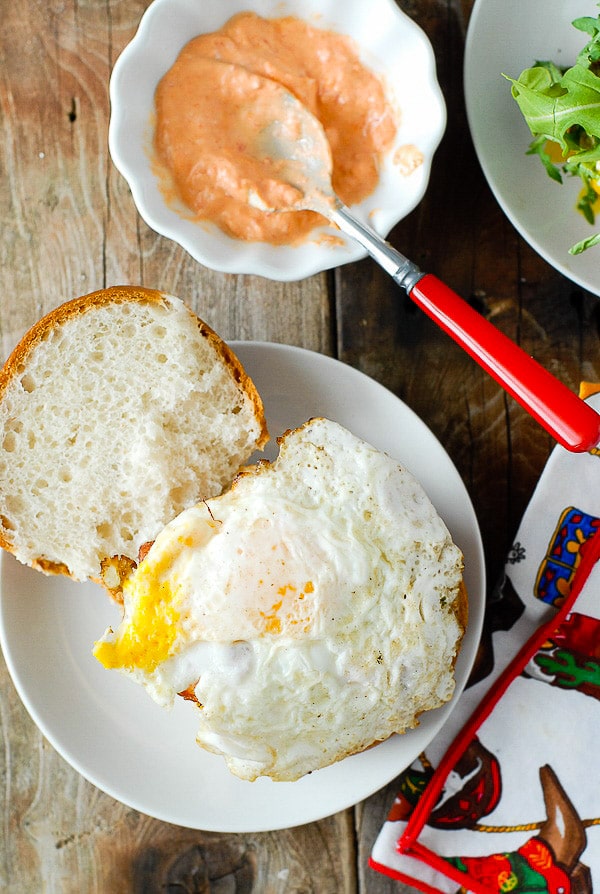 Freshly fried egg on top of a grilled hamburger, gluten-free bun on a white plate