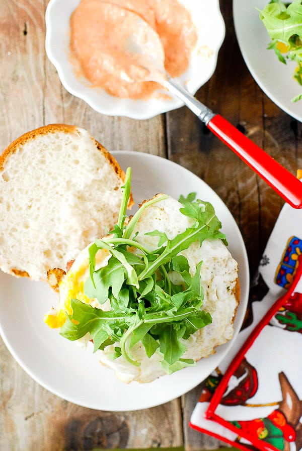 Fresh arugula on top of a fried egg Breakfast Burger with Sriracha Sour Cream on a white plate 