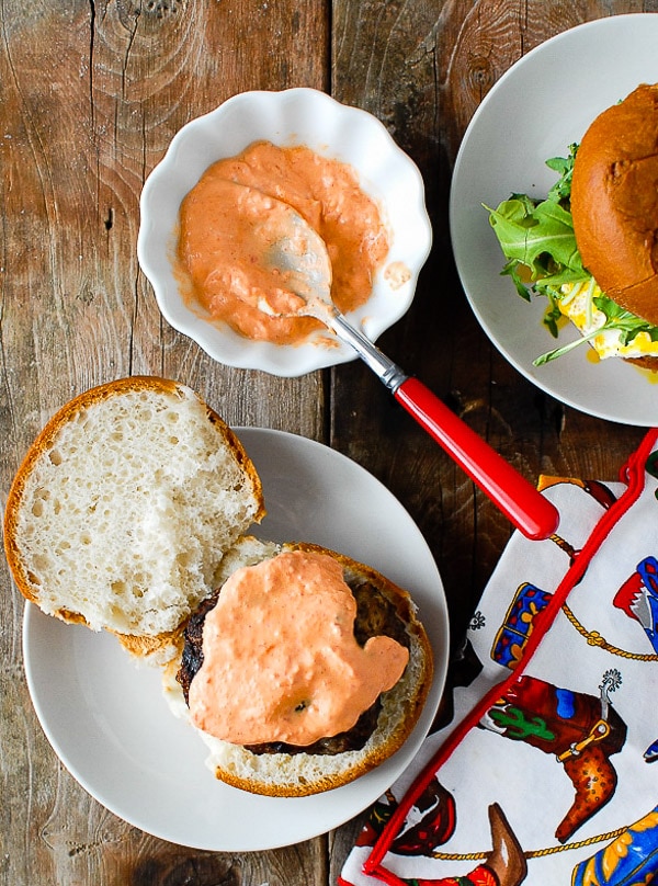 Grilled burger with homemade Sriracha Sour Cream sauce on a gluten-free bun with cowboy napkin on a white plate